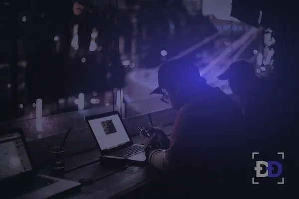 People work on laptops at a window counter at night with city lights outside.